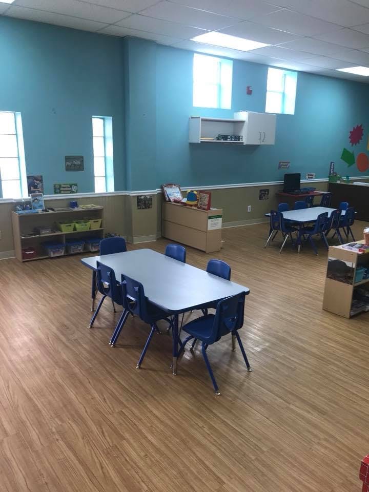 Classroom with blue walls, light wood floor, and small tables with blue chairs