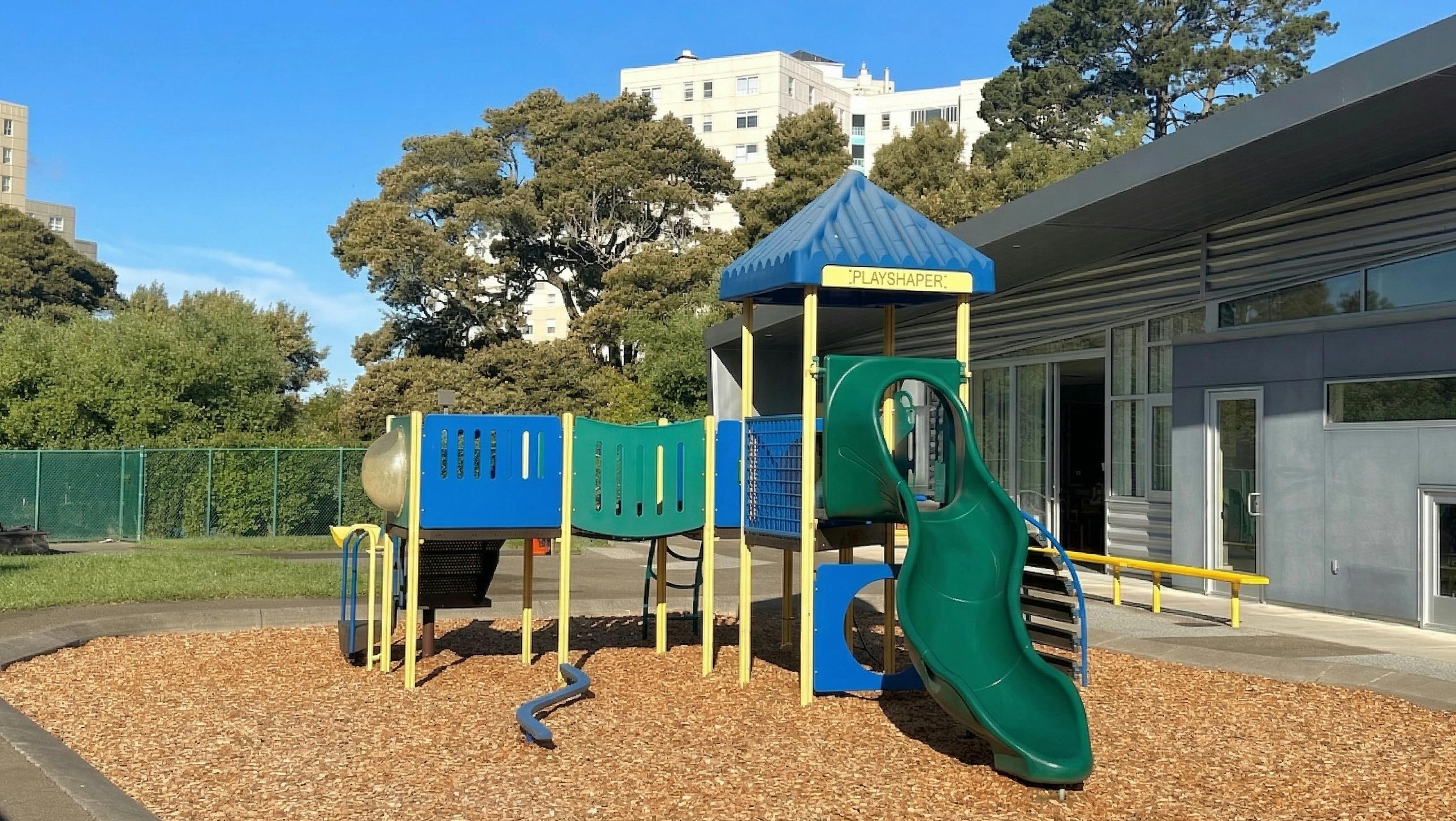 A colorful playground with a slide and climbing structure on wood chips
