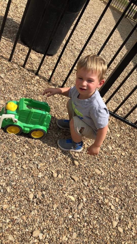 Child crouching next to a green toy truck on gravel