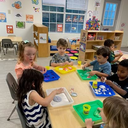 Group of children playing with modeling clay at a table in a classroom