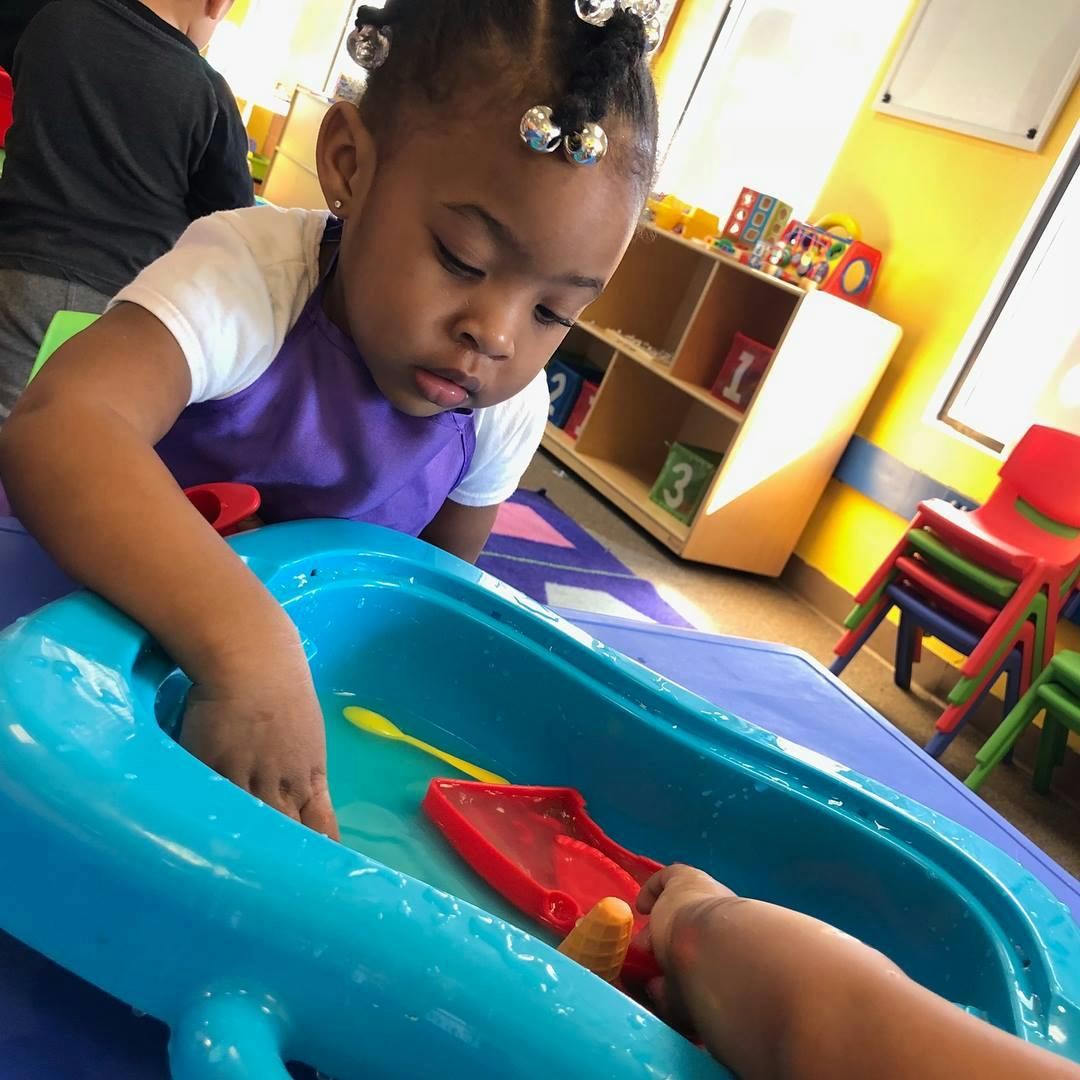 Child playing with water in a blue bin