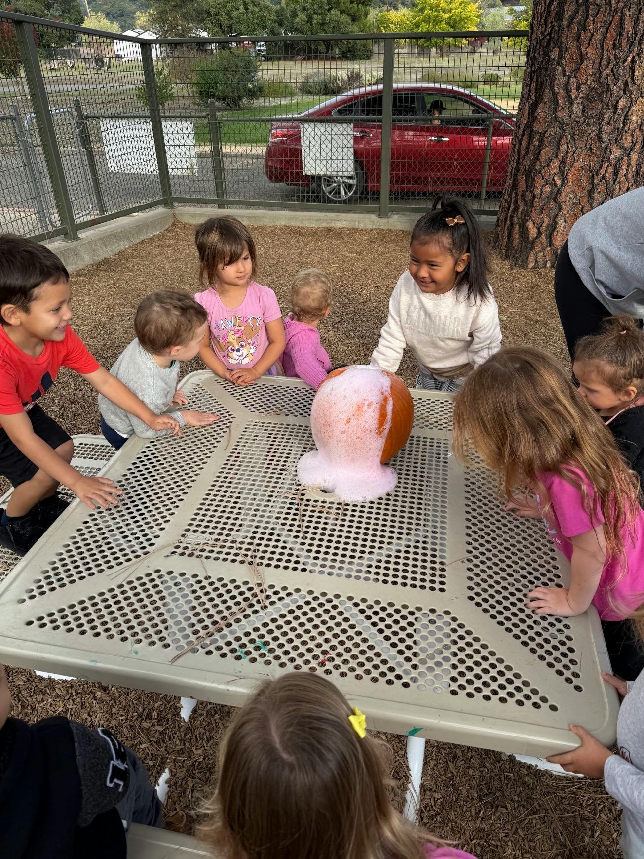 Children gathering around a table with a pumpkin erupting with foam