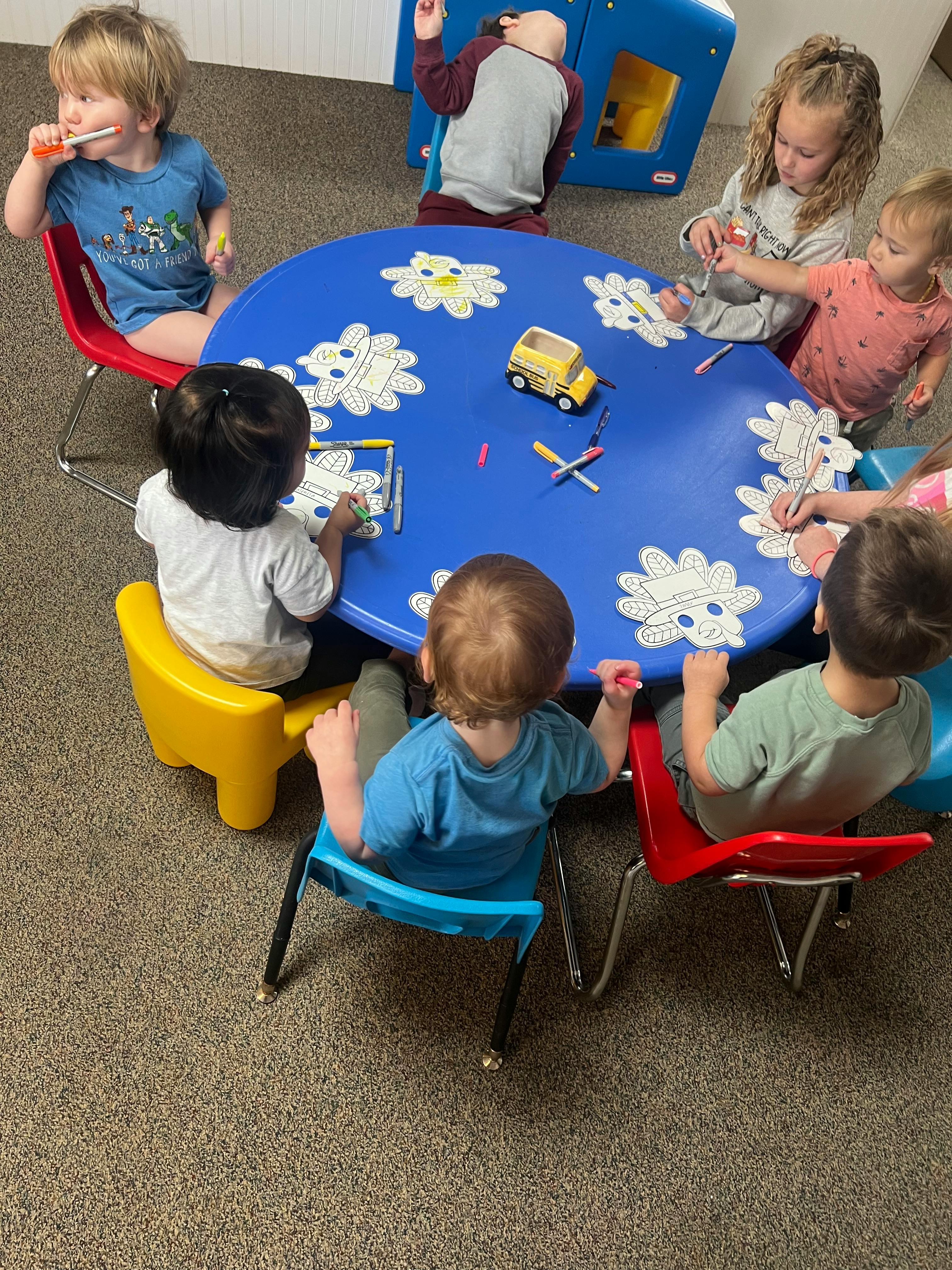 Children sitting around a blue table with coloring pages and toys