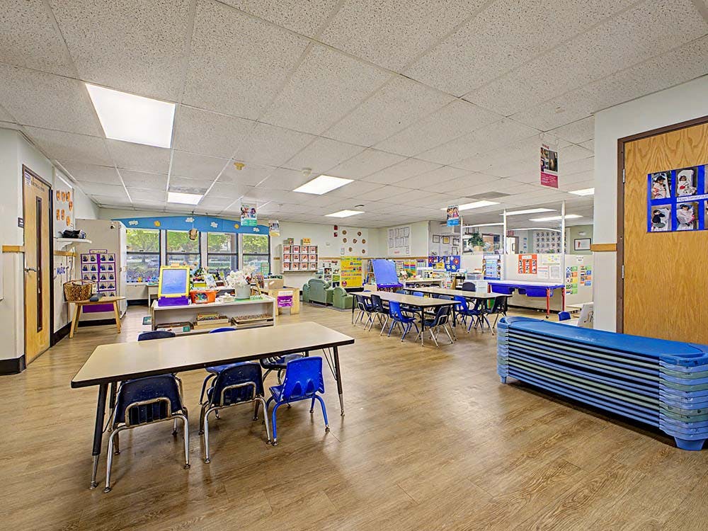 Empty preschool classroom with tables, chairs, and cots