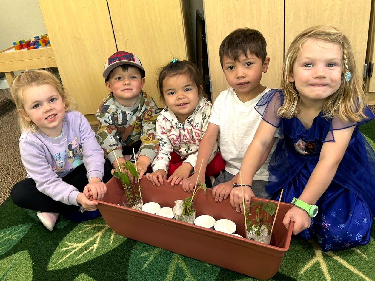 Five children kneeling around a planter with small plants