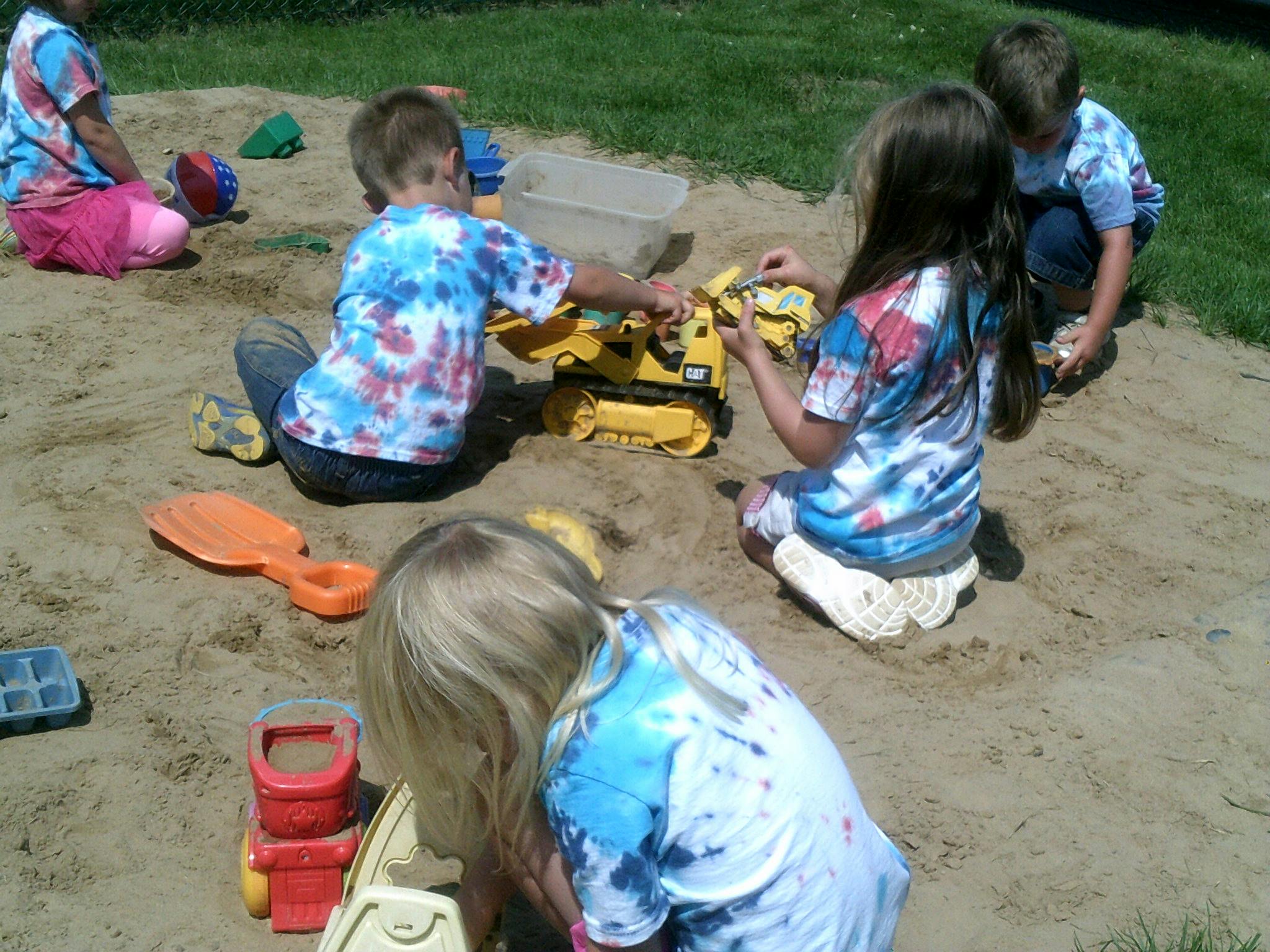 Children playing in a sandbox with toy construction vehicles