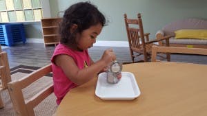 Child playing with a can and tray at a table