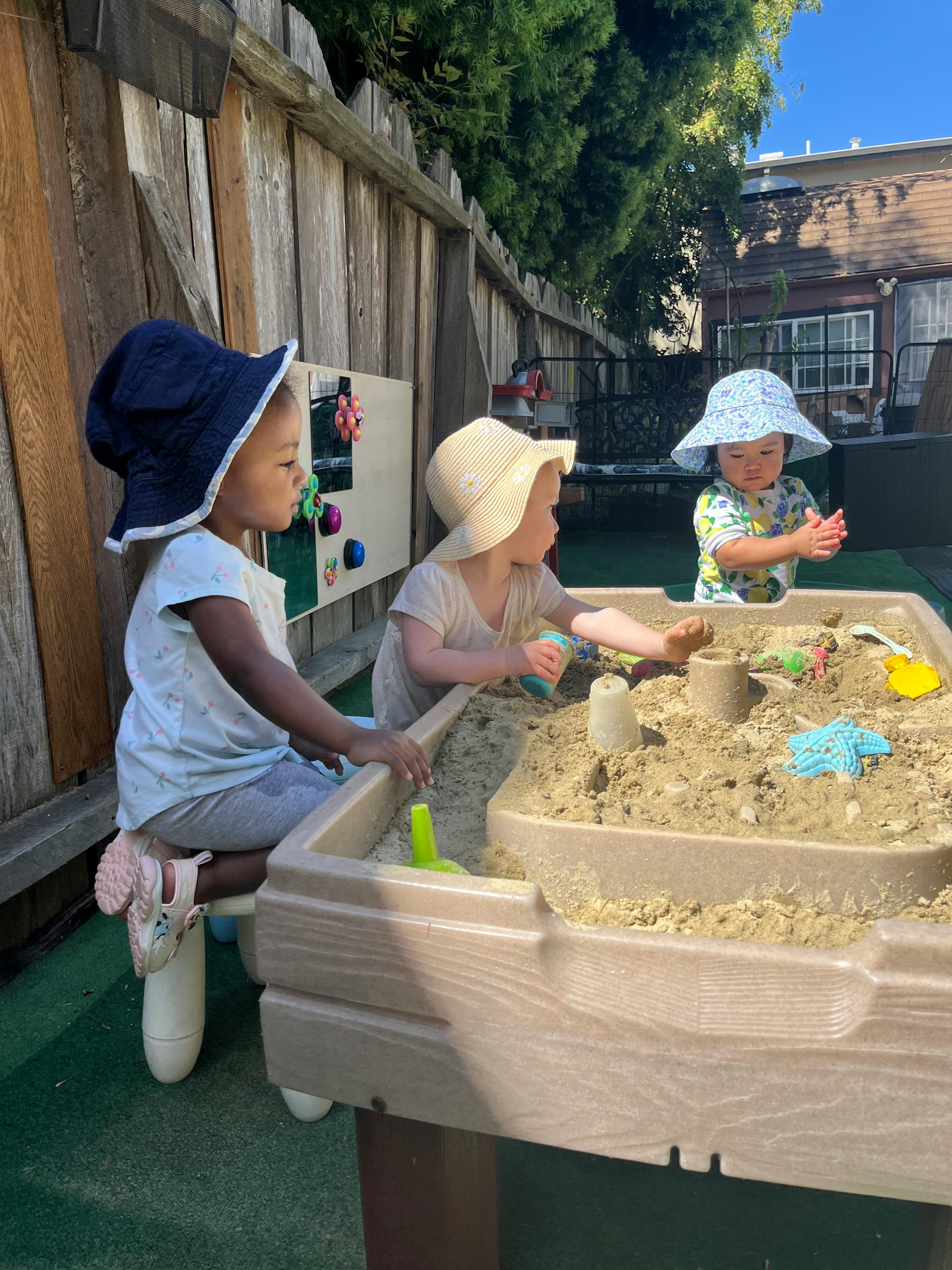 Three children playing in a sandbox outdoors