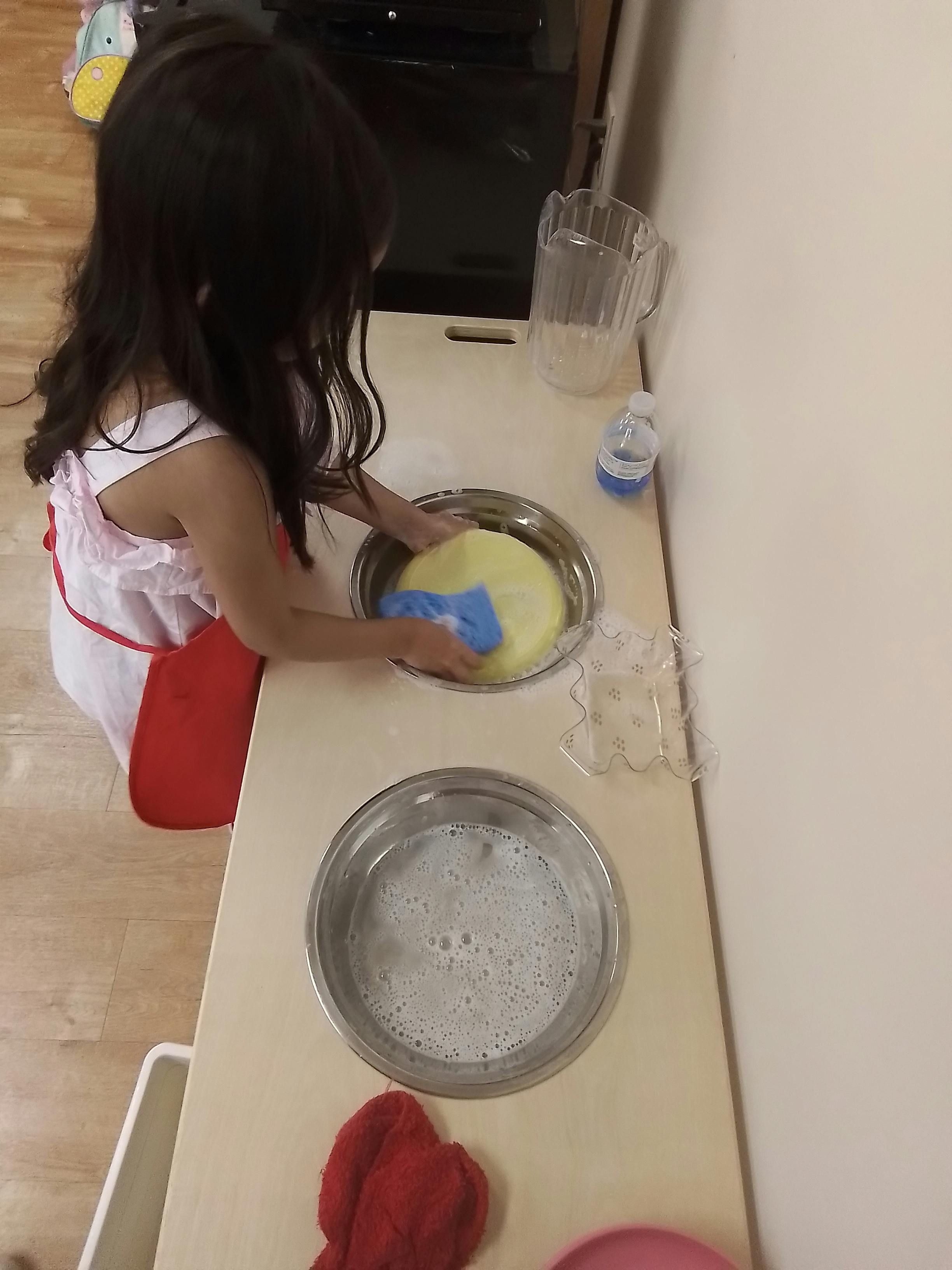 Child washing a yellow object in a bowl with a blue cloth