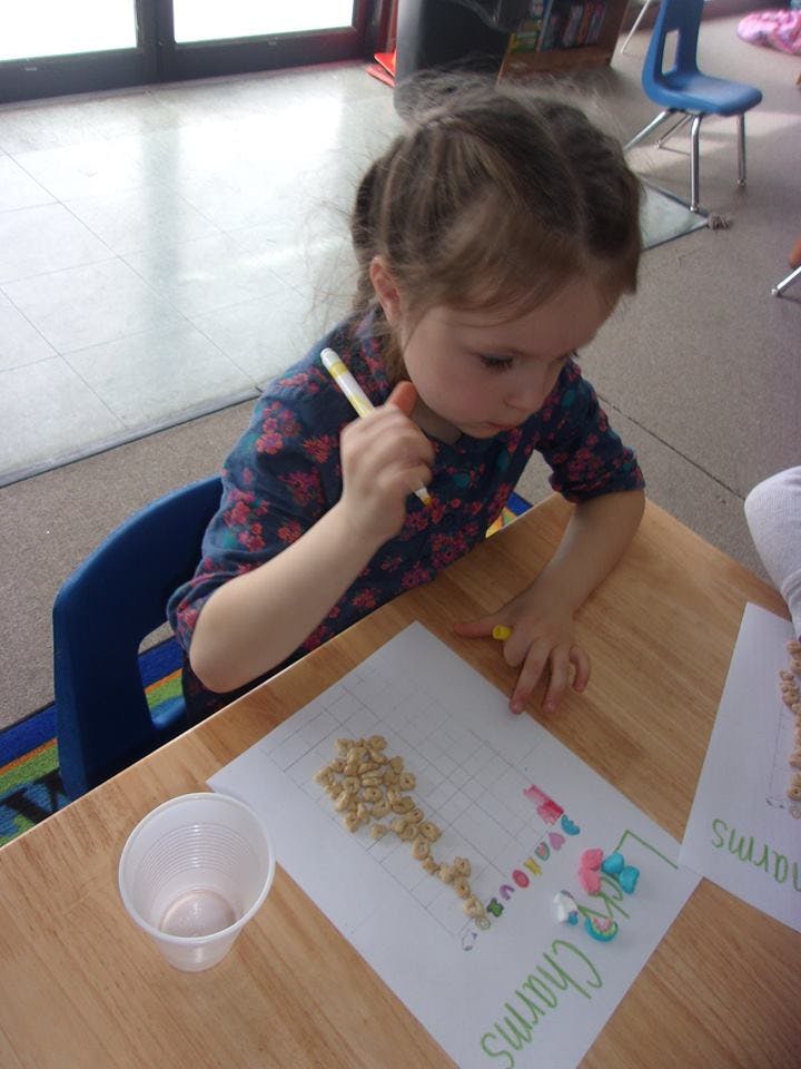 Child at a table working on a craft with cereal pieces