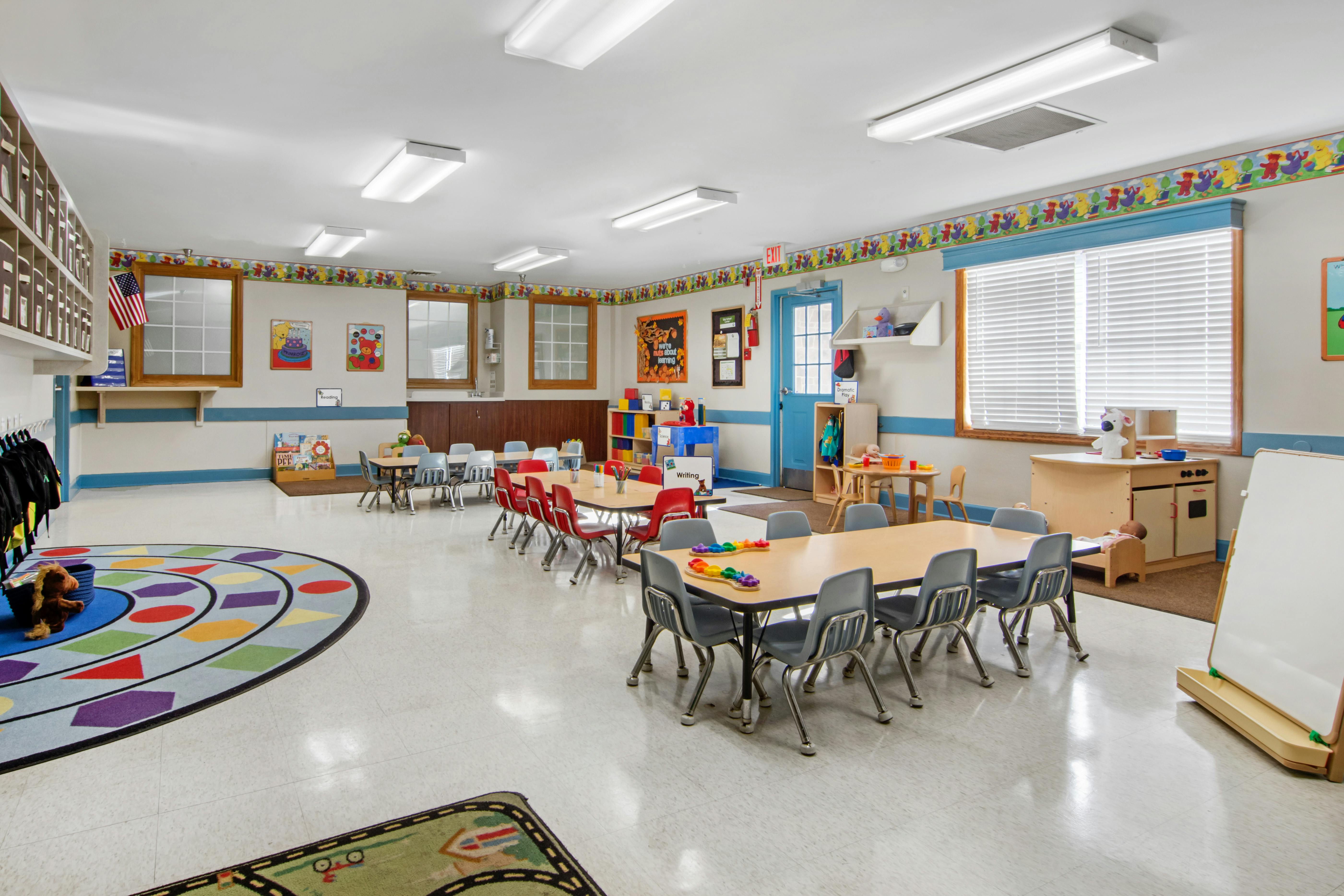 Classroom with small tables and chairs, colorful rugs, and play areas