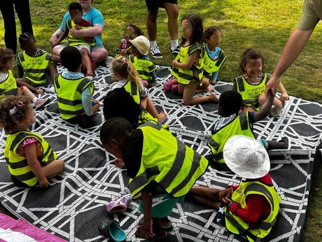 Many children and adults sitting on a patterned blanket outdoors