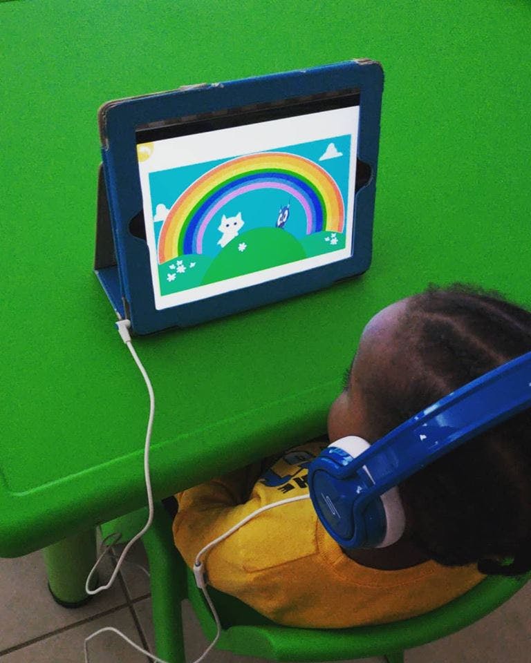 Child wearing headphones watching a tablet displaying a rainbow