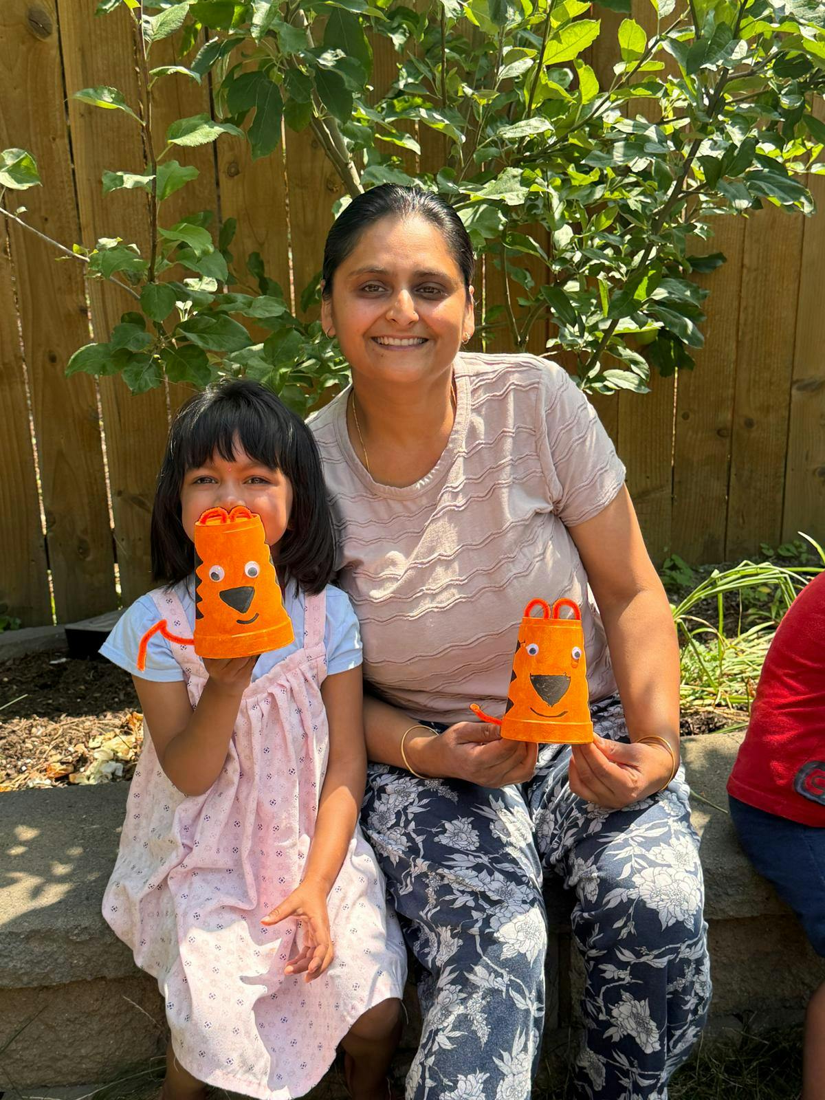 A person and a child holding tiger-themed paper cup crafts