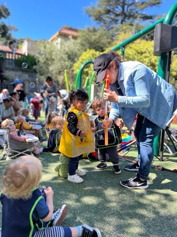 Person in a cap blowing bubbles for children in a playground
