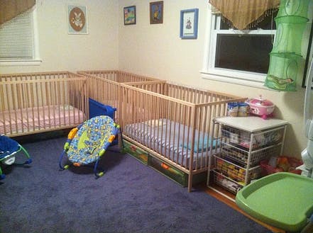 Three cribs in a room with a baby bouncer on the floor
