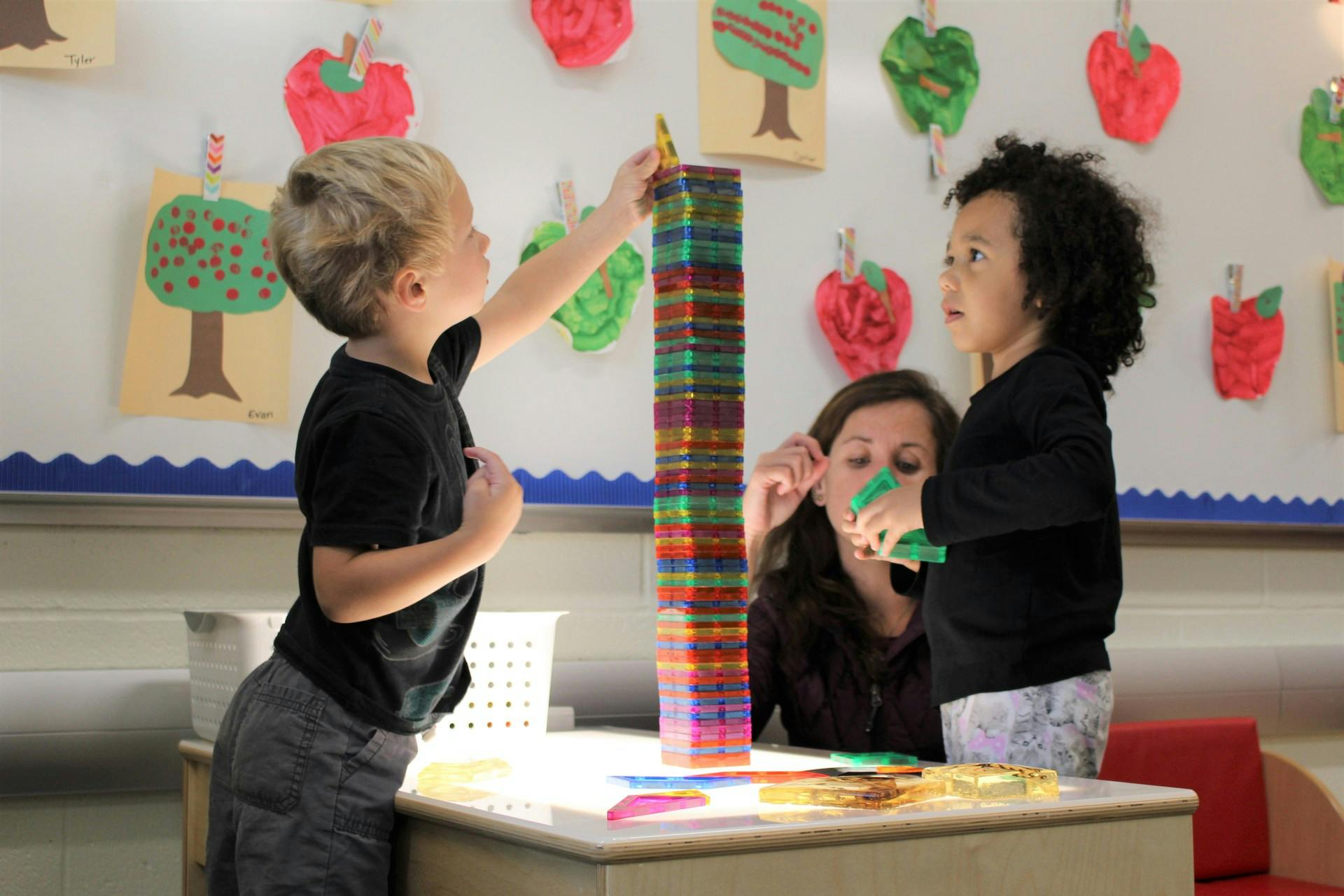 Three people building a tall tower with colorful blocks on a table