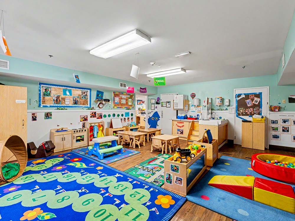 Colorful classroom with small tables and chairs, play mats, and toys