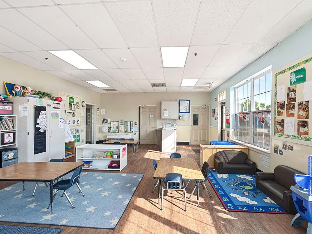 A classroom with tables, chairs, a blue rug with stars, and a window