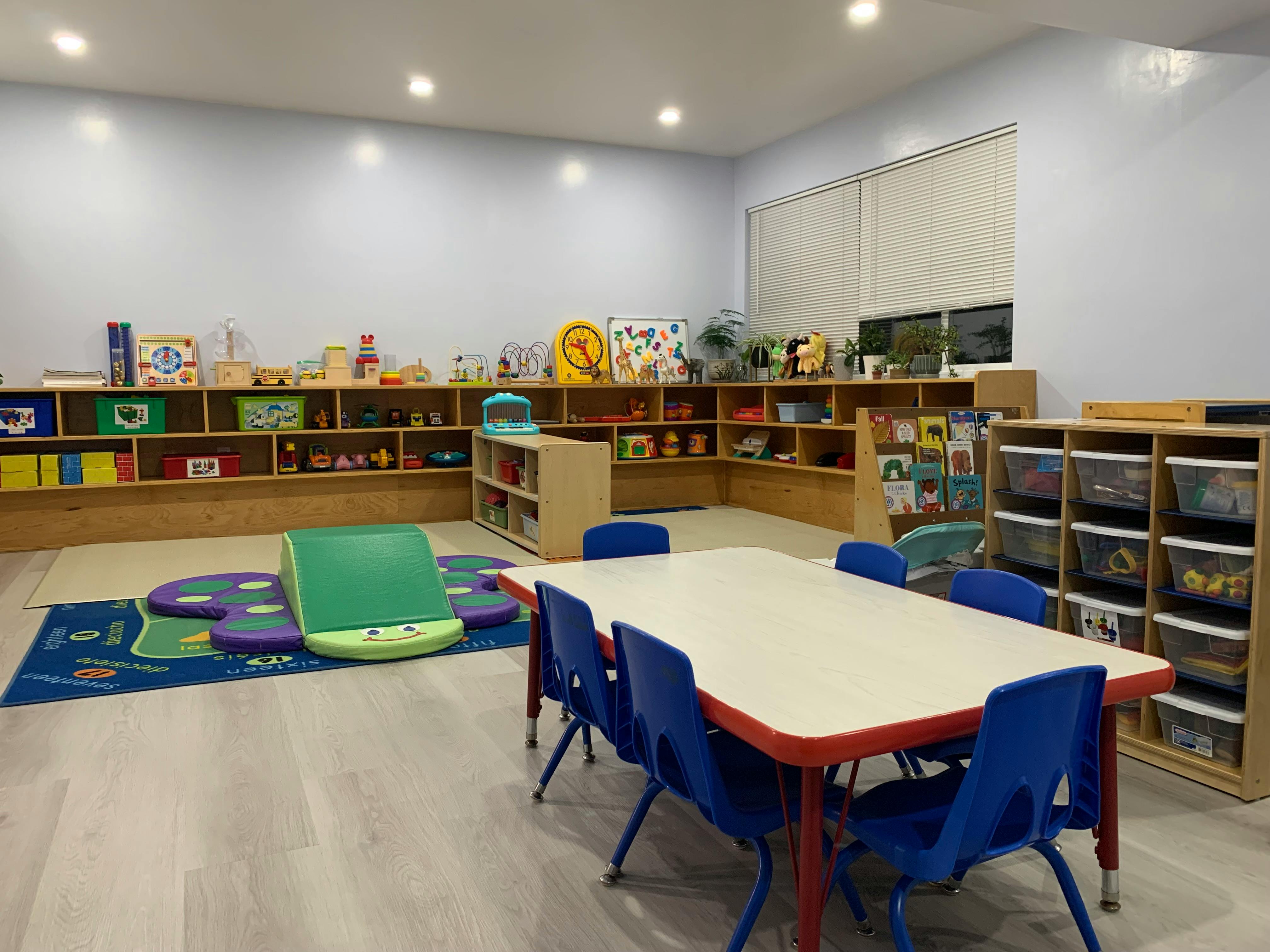 Empty classroom with tables, chairs, and shelves filled with toys and books
