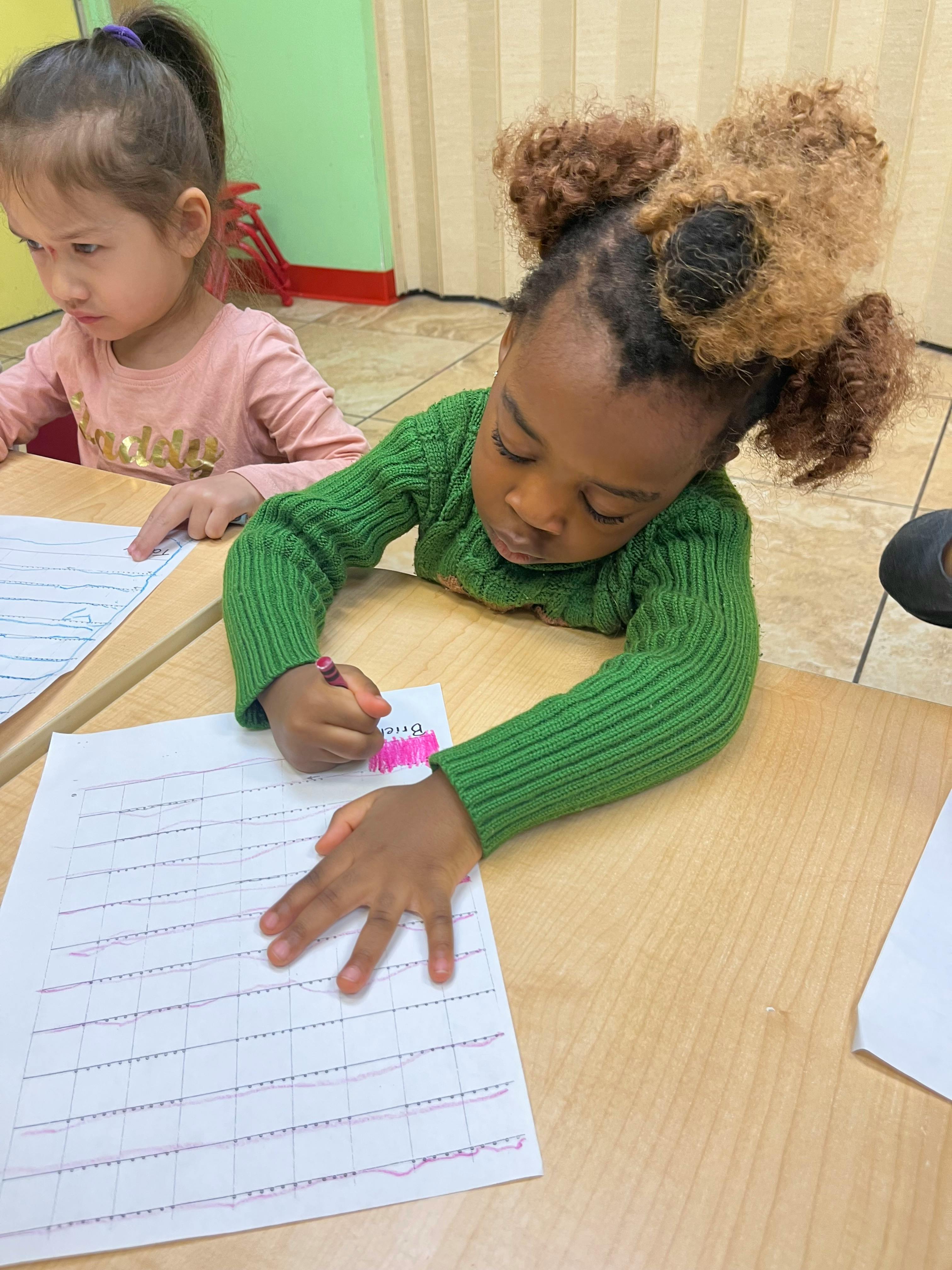 Two children sitting at a table, one coloring on a paper