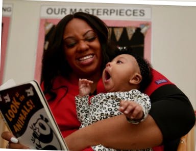 Person holding a child who is yawning while reading a book