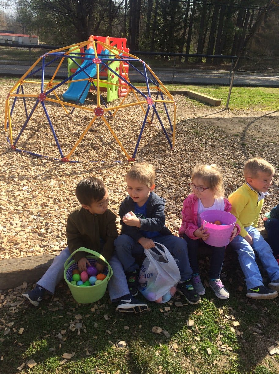 Children sitting on ground with baskets of colorful eggs on a playground