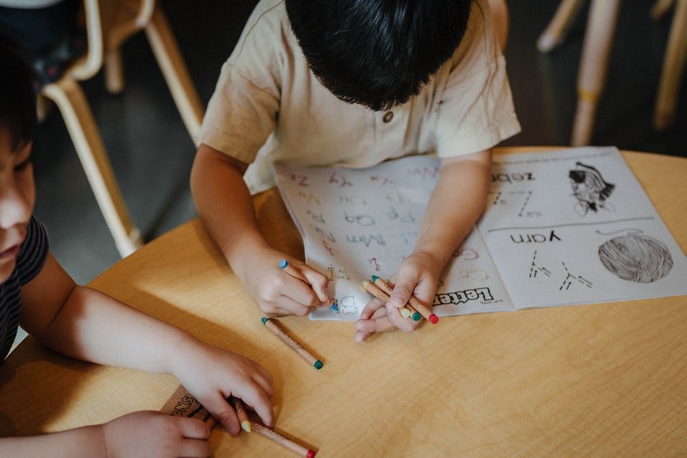 Child learning to write letters and another child's hands holding crayons