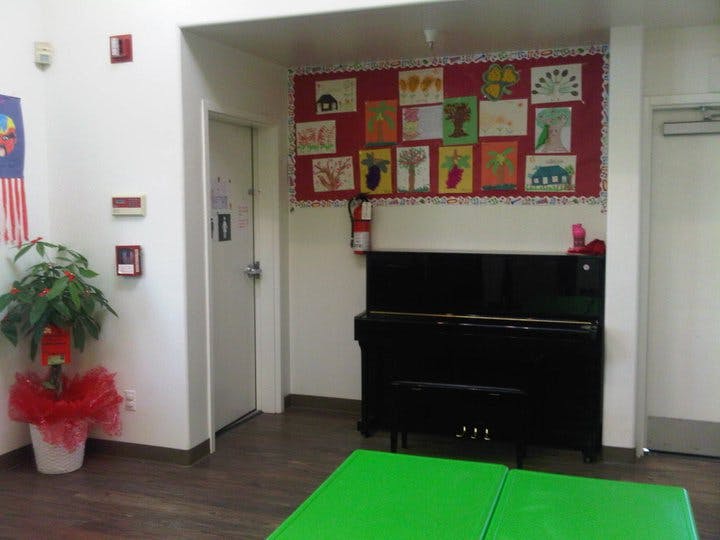 Black piano under a bulletin board with children's drawings