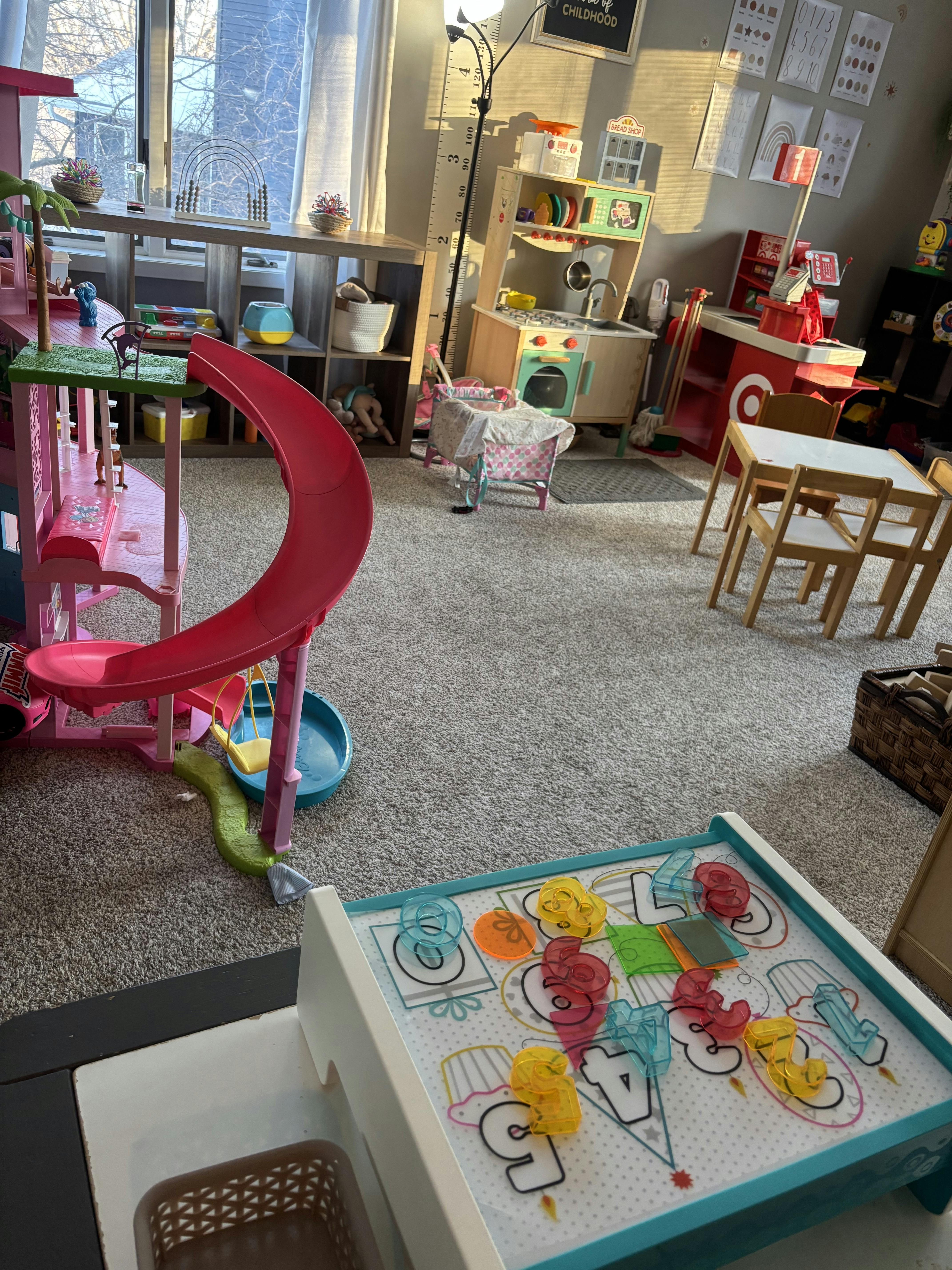 Dollhouse, play kitchen, and small table with chairs in a child's play area