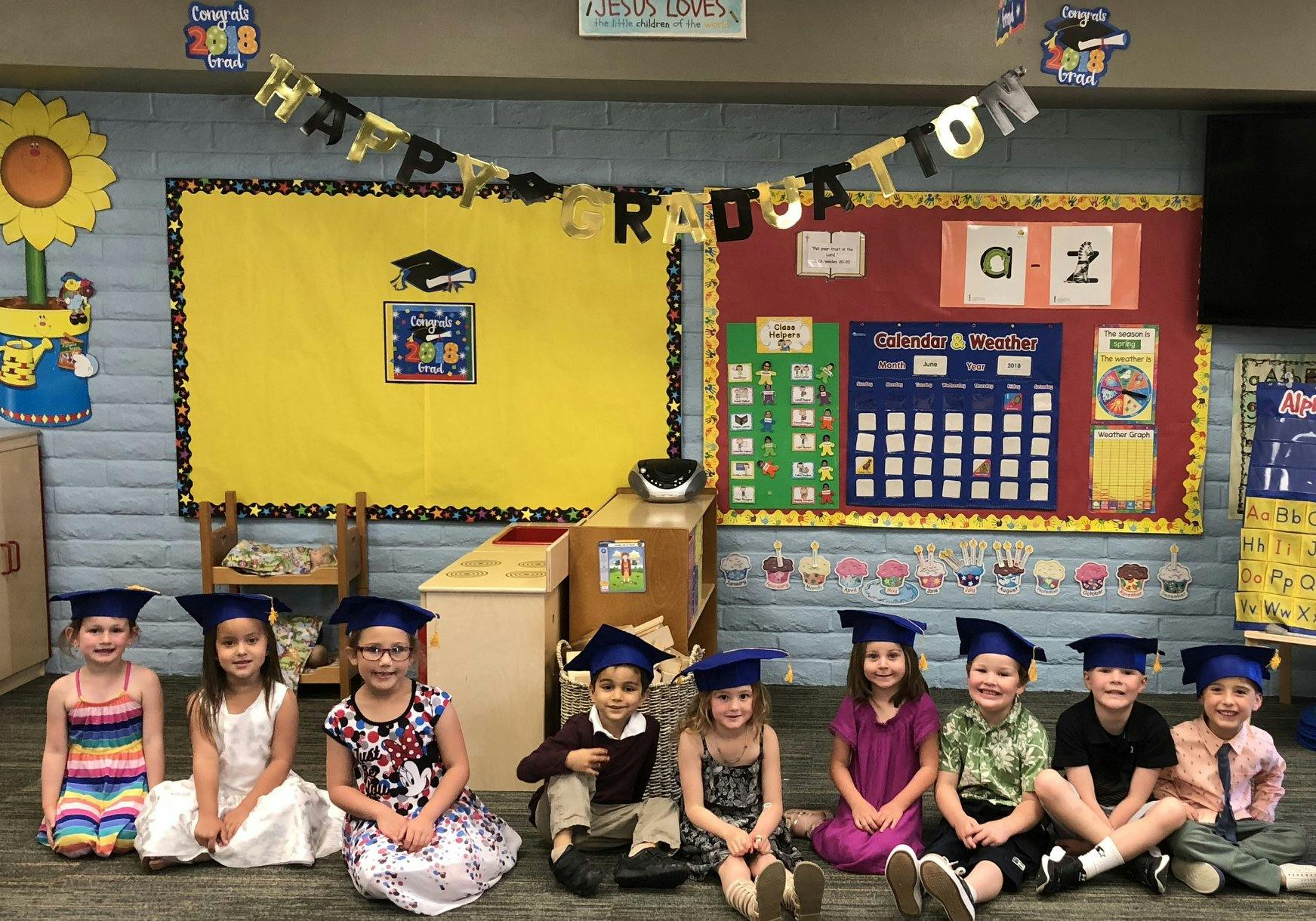 Children wearing graduation caps sitting on the floor in a classroom