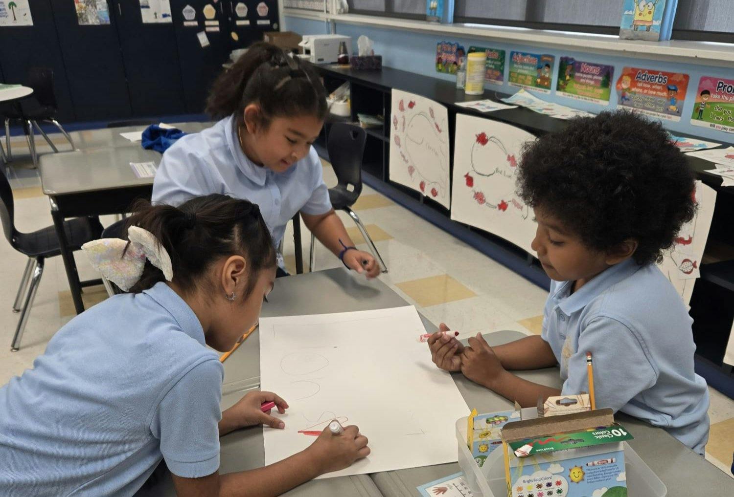 Three children drawing on paper at a classroom desk