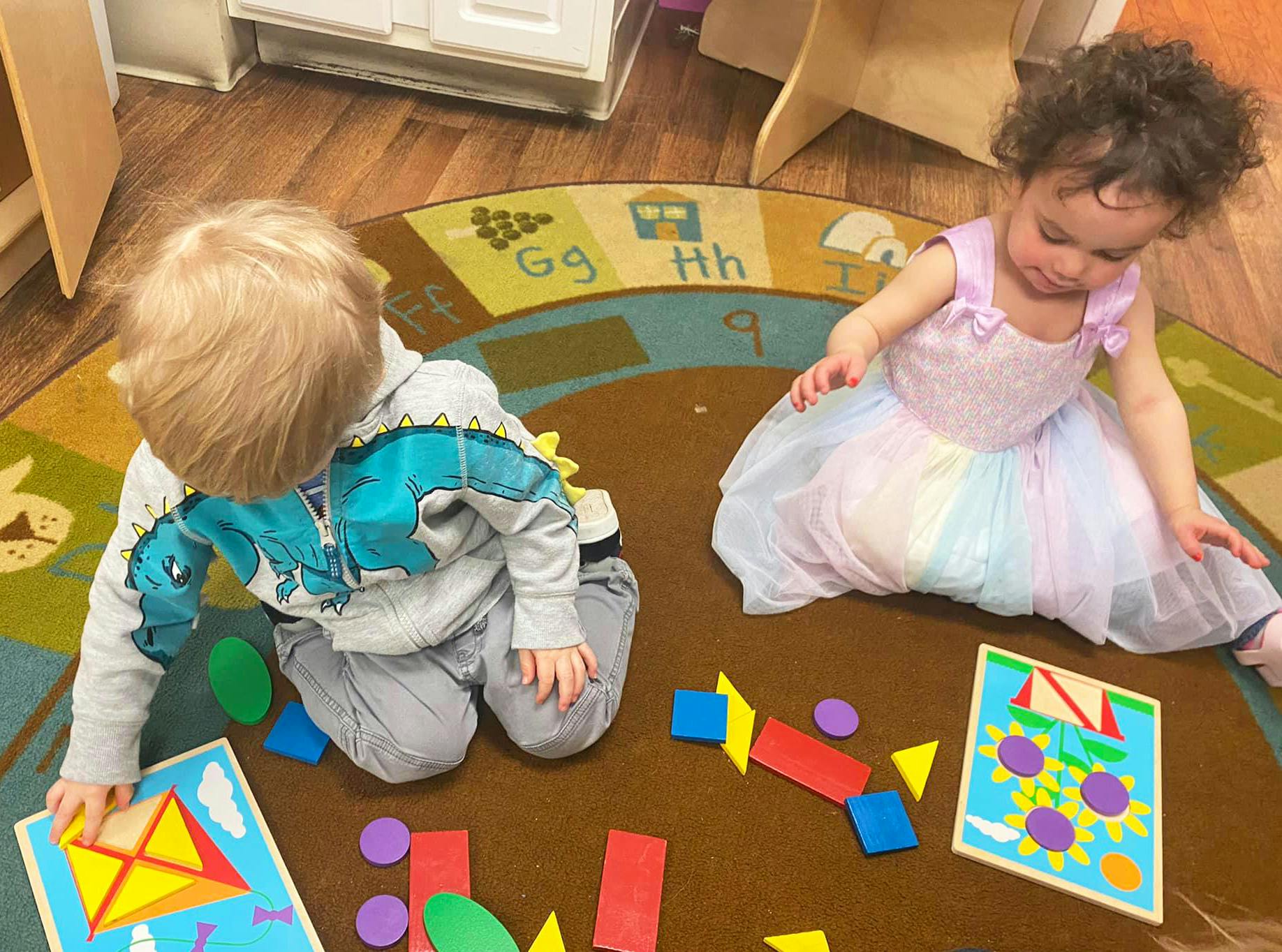 Two children playing with shape puzzles on a rug