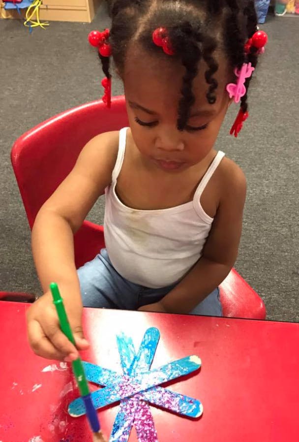 Child painting a craft on a red table