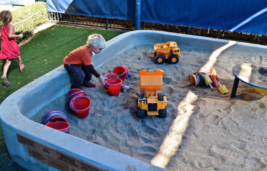 Child playing in a sandbox with toy trucks and buckets