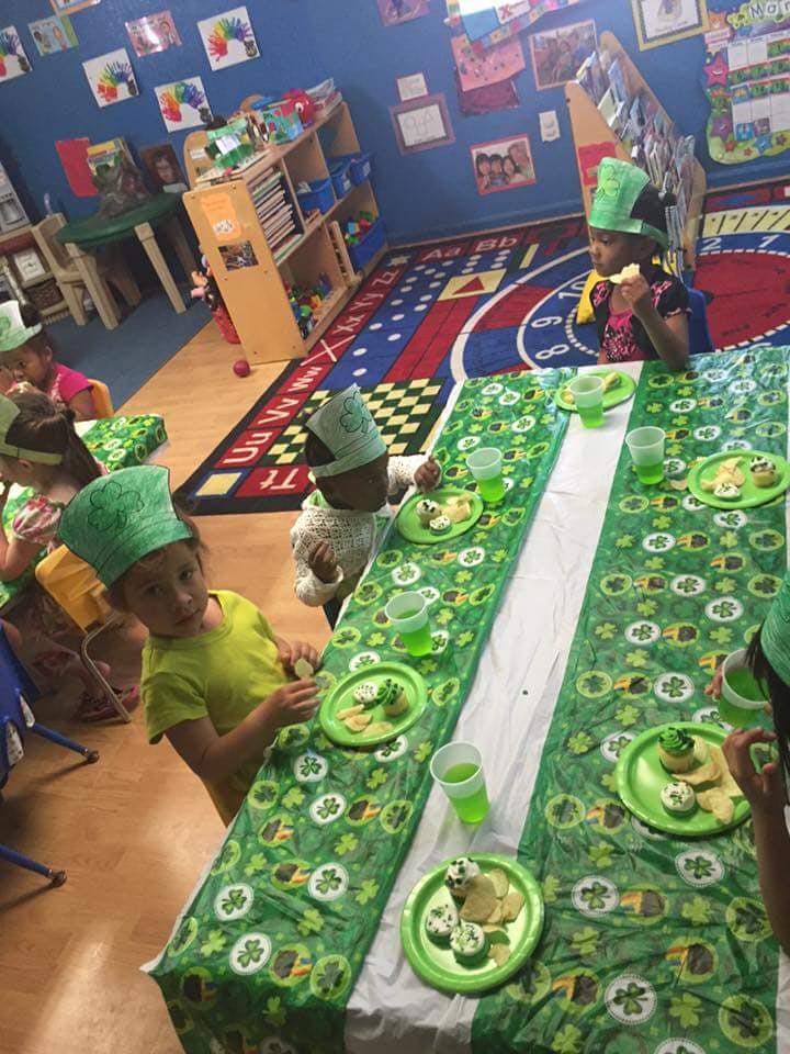 Children wearing green hats eating at a table in a classroom
