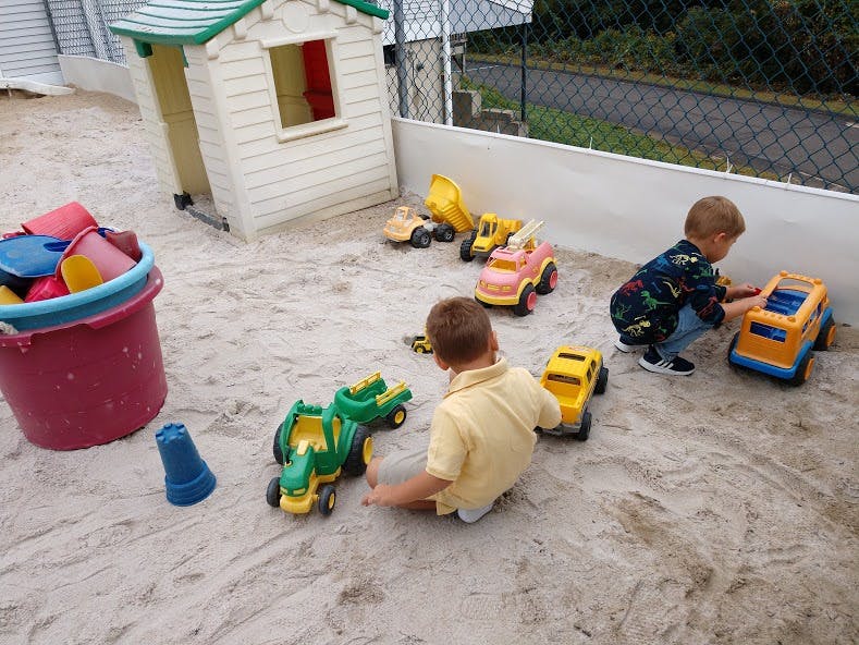 Two children playing with toy trucks in a sandbox