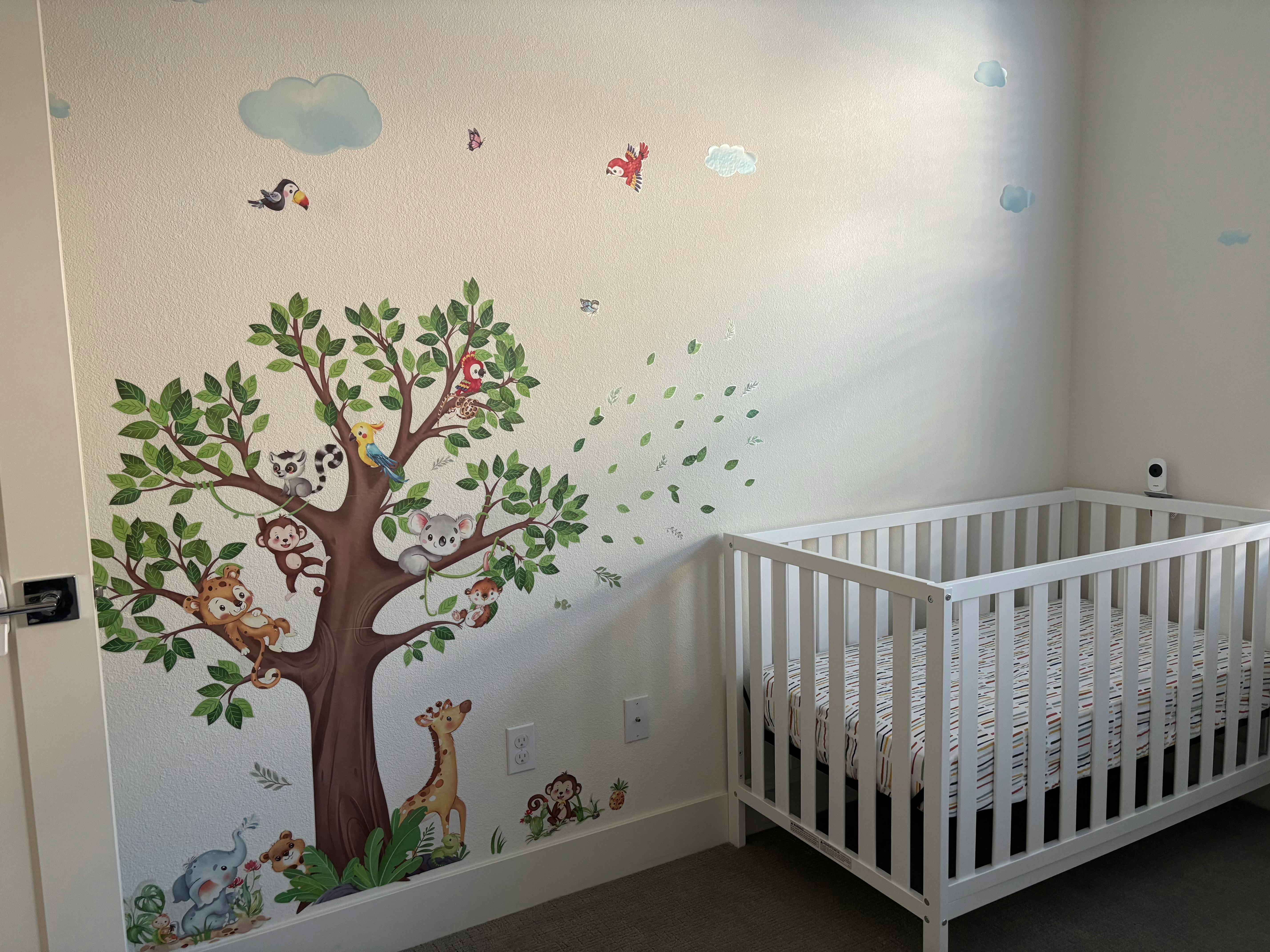 Nursery room with a white crib and a wall decal of a tree with animals