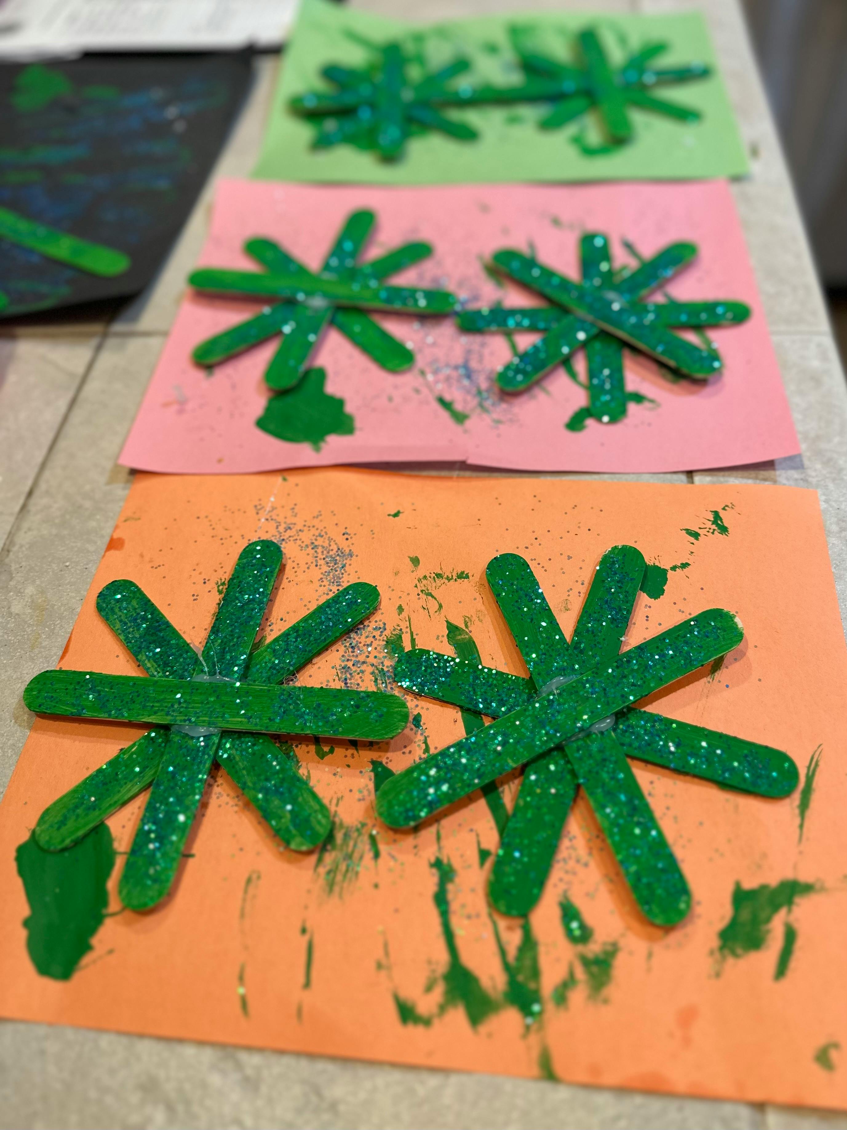 Crafts made from green popsicle sticks arranged in star shapes on colored paper