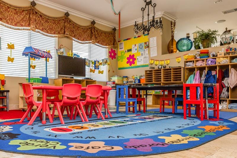 Preschool classroom with small red tables and chairs, blue rug with letters