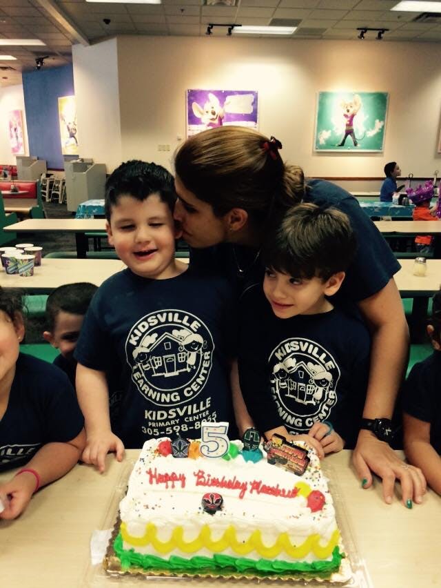 Person kissing a child on the cheek next to a birthday cake with a number 5 candle