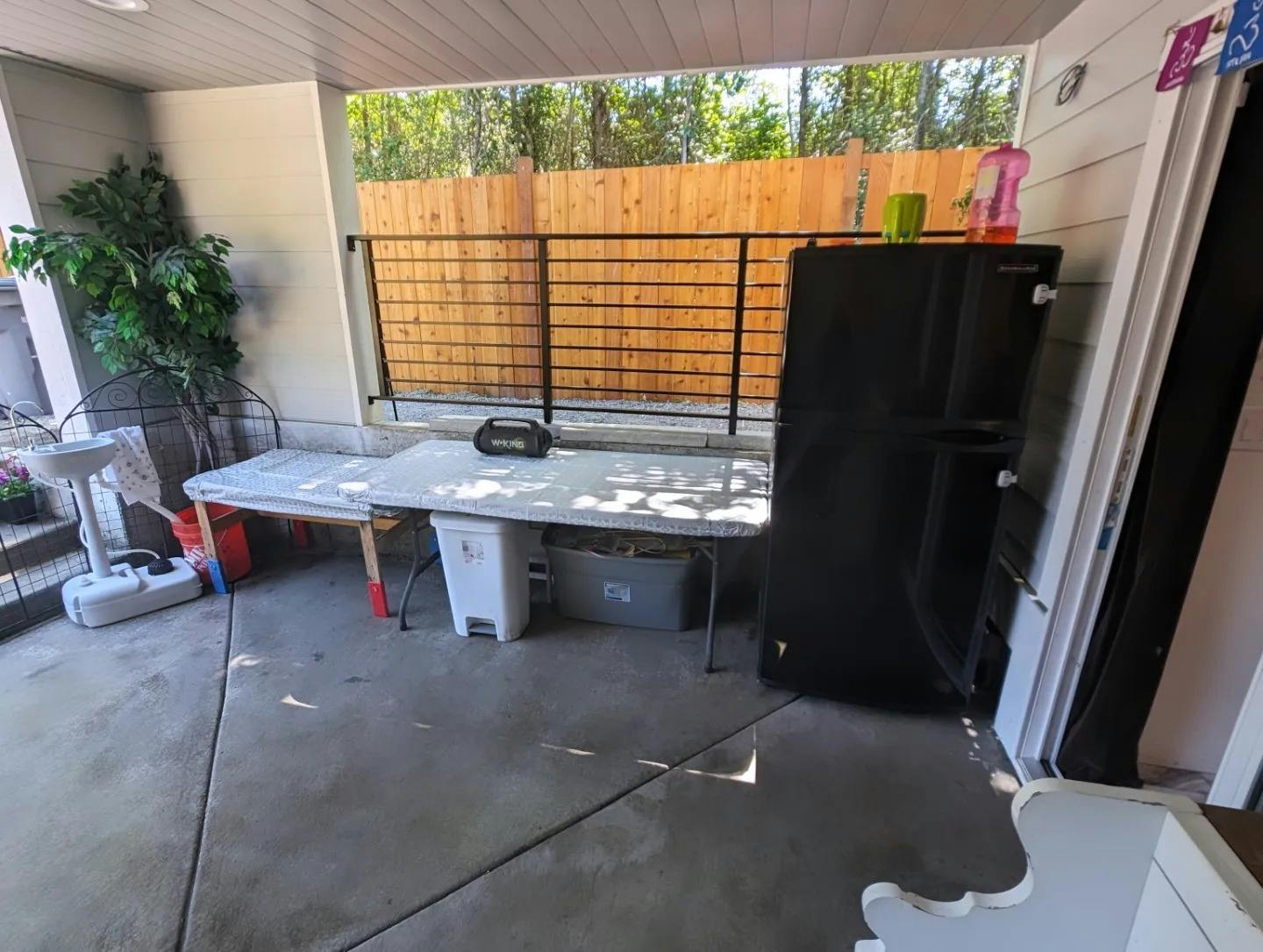 Outdoor patio with a long table, a black refrigerator, and a plant