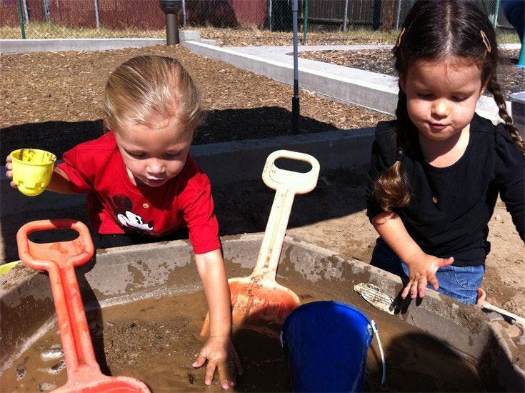 Two children playing in a sandbox with toys