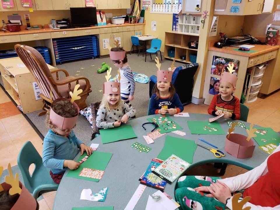 Children wearing antler headbands doing crafts at a table in a classroom