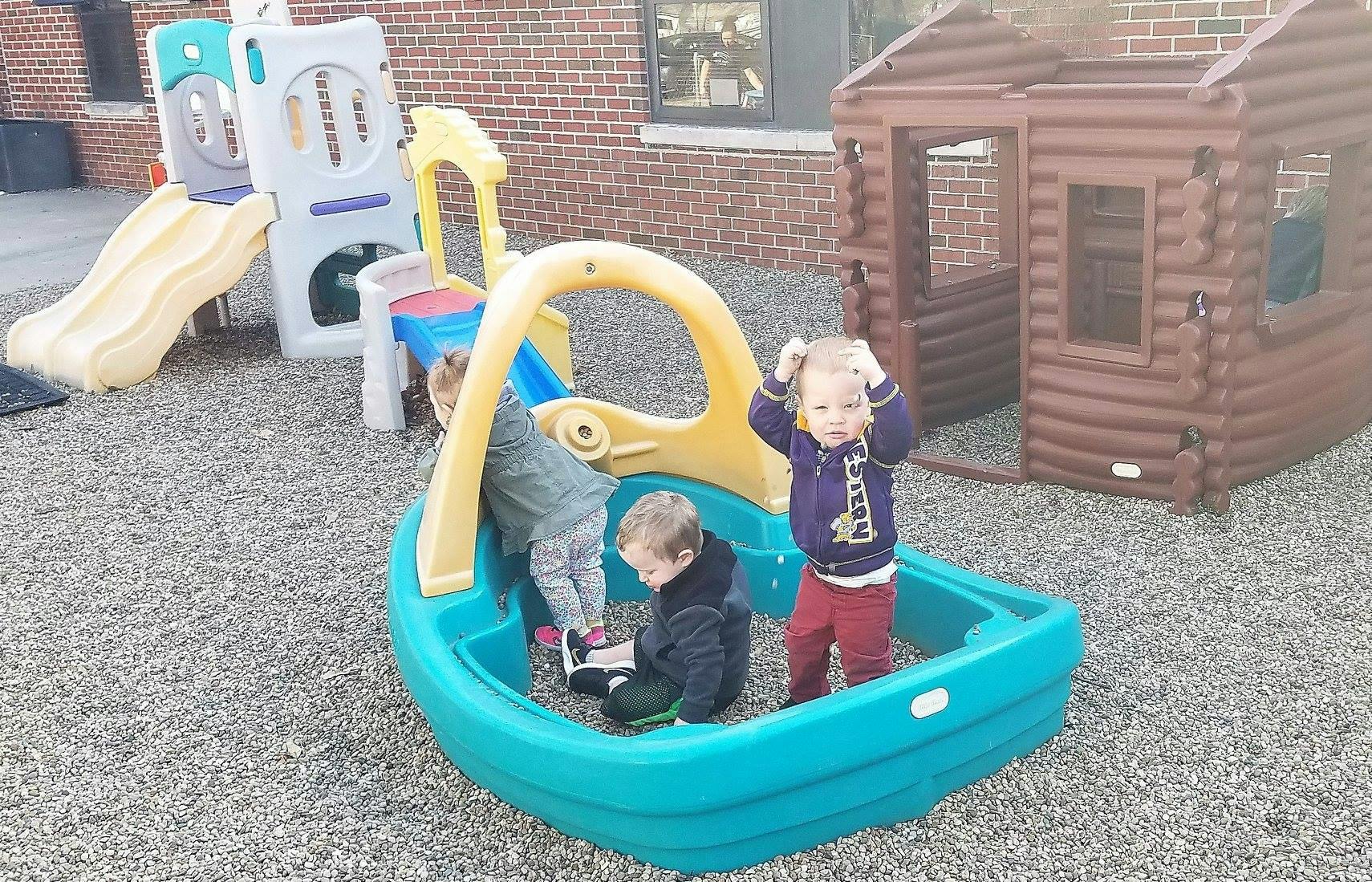 Three children playing in a sandbox and on playground equipment