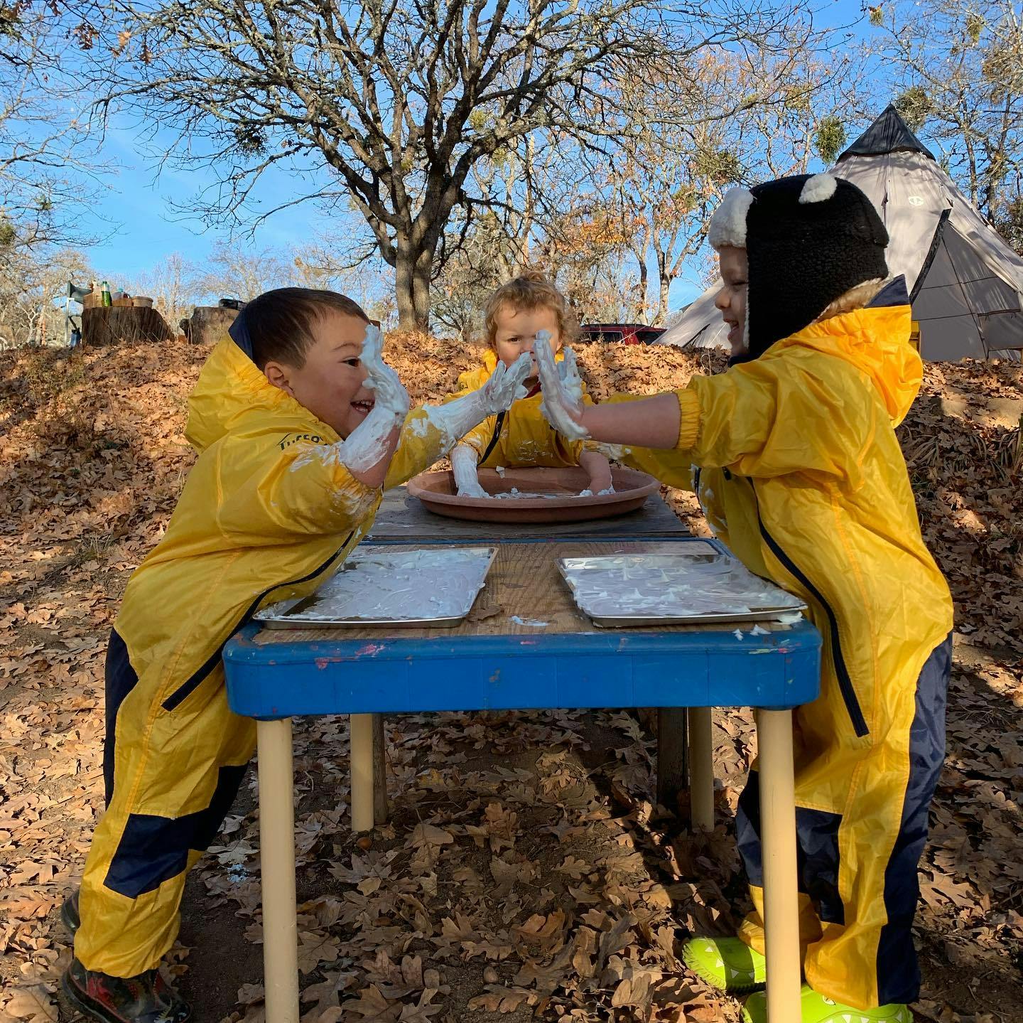 Children in yellow rain suits playing with white material on a table outdoors