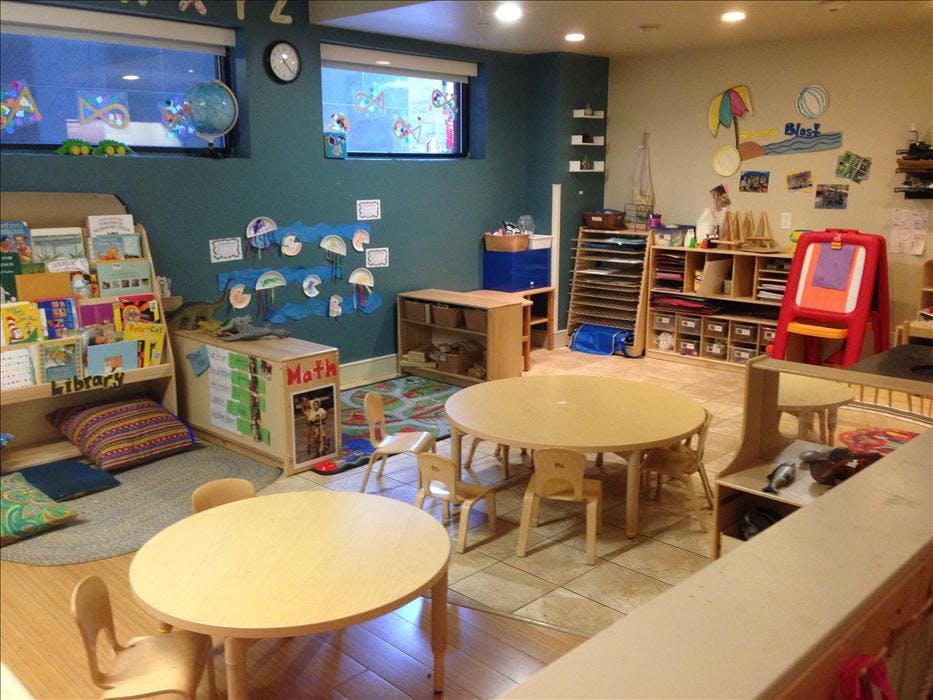 A colorful classroom with small tables and chairs, a bookshelf, and various learning materials