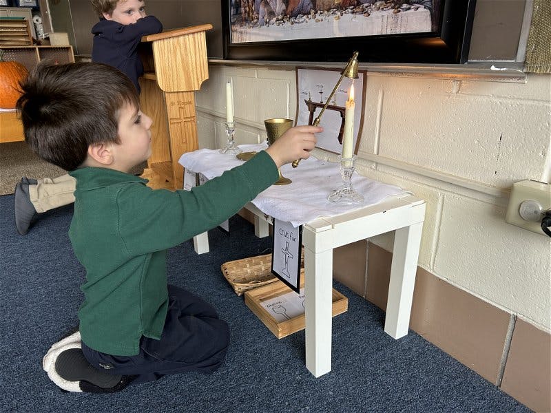 Child kneeling and lighting a candle on a small table