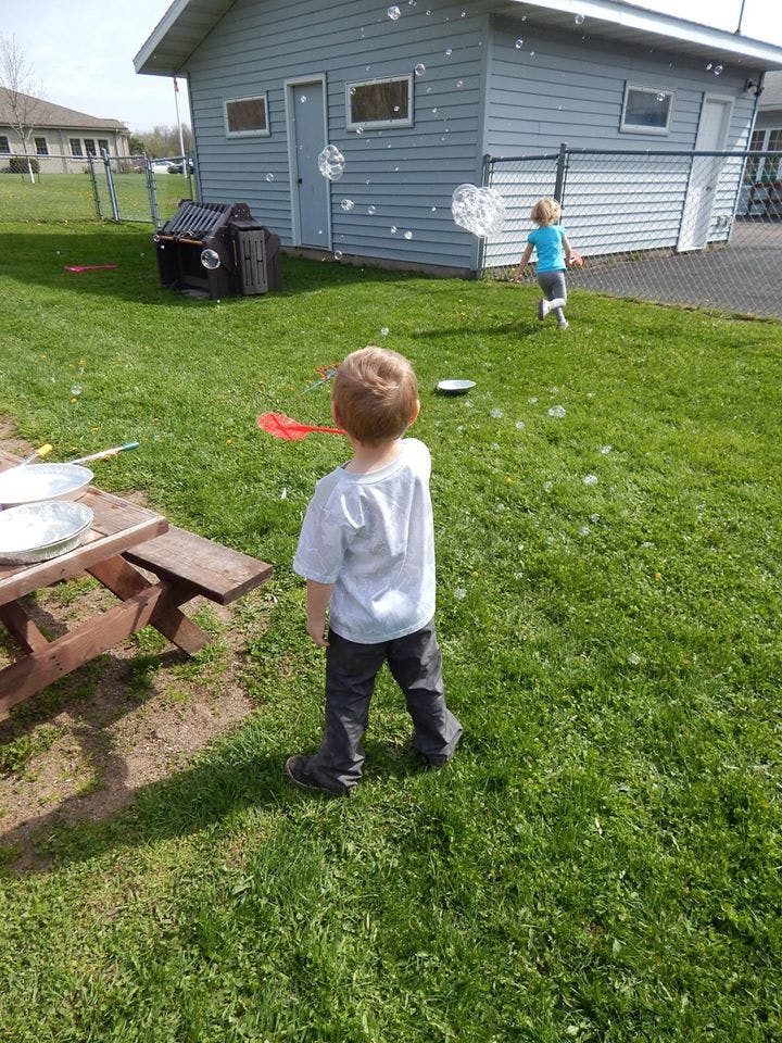 Child blowing bubbles in a grassy yard