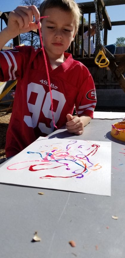 Child holding a string over a paper with colorful paint